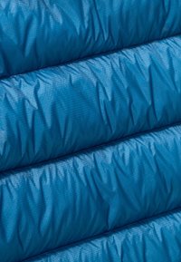 Tessuto isolante blu con una superficie morbida e testurizzata, caratterizzato da sezioni cucite e un sottile motivo a griglia su tutto il materiale.