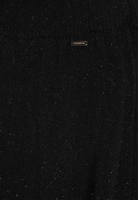 Fekete kötött pulóver puha, textúrált anyagból. Kis arany logótartóval rendelkezik. A kialakítása egyszerű, minta vagy további díszítések nélkül.