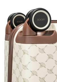 Walizka na kółkach o teksturowanej kremowej powierzchni z delikatnym wzorem. Brązowe akcenty i czarne kółka z białymi detalami.