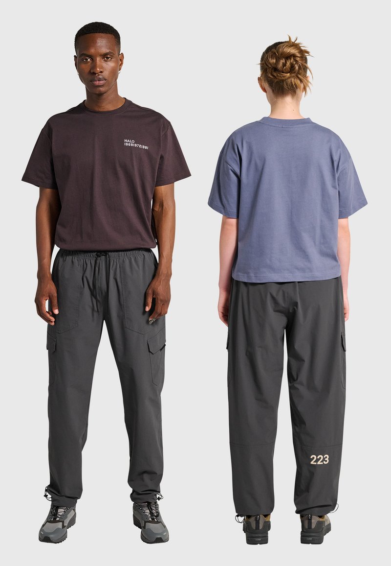 Mężczyzna zwrócony przodem, ubrany w ciemny t-shirt i spodnie bojówki, kobieta zwrócona tyłem, ubrana w niebieski t-shirt i ciemne spodnie bojówki z napisem "223".