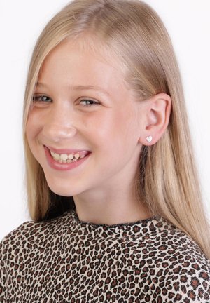Ohrringe aus Sterling Silber in Herzform, klein und glänzend, getragen von einem Mädchen mit langen, glatten blonden Haaren, das ein Oberteil im Leopardenmuster trägt.