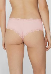 Světlé růžové bokové kalhotky s krajkovým lemováním, vyrobené z hladkého, elastického materiálu se zvlněnými okraji. Krajka dodává jemnou texturu v pase.