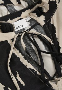 Tessuto stampato nero e beige con chiusura a cravatta al collo; presenta bordi arricciati e un'etichetta che indica il marchio e la taglia.