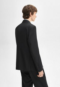 Zwarte blazer met een gestructureerd ontwerp, enkele achteropening en tweeknoopsluiting. Gladde stof, getailleerde pasvorm en lange mouwen.