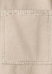Gros plan d'une poche en tissu beige avec des coutures visibles sur un fond de matériau texturé.