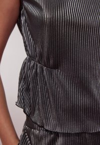 Top senza maniche in tessuto nero con strisce verticali argento. Presenta un design a strati e un orlo arricciato lungo la vita per un tocco di texture.