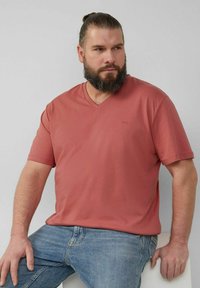 T-Shirt mit kurzen Ärmeln und V-Ausschnitt in Korallenrot, aus weicher Baumwolle gefertigt, mit kleinem Logo auf der Brust und lässigem Schnitt, kombiniert mit blauen Jeans.