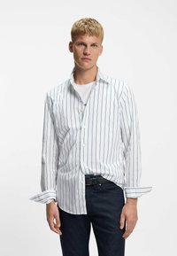 Wit overhemd met verticale marineblauwe strepen, katoenen materiaal, lange mouwen, losse pasvorm, gecombineerd met donkere spijkerbroek en een riem.