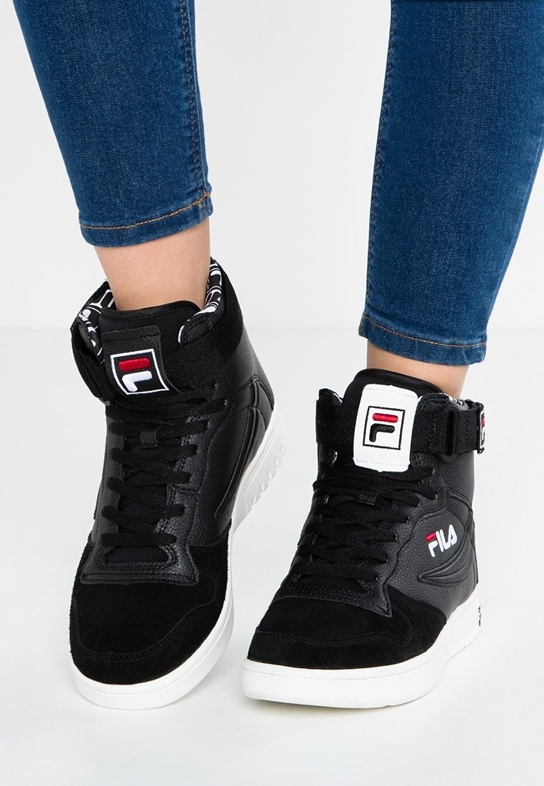Baskets montantes noires Fila avec semelles blanches portées avec un jean bleu, dotées de lacets et de patchs de marque sur les languettes et les côtés.