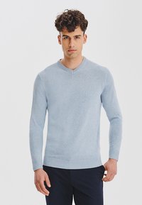 Jasnoniebieski sweter w serek z miękkiego materiału z długimi rękawami. Posiada ściągacz na dolnym obszyciu i mankietach, gładką fakturę oraz dopasowany krój.