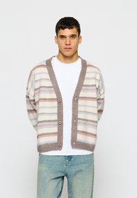 Črtast kardigan iz mehke tkanine, ki ima vodoravne črte v bež, svetlo modri in roza barvi, s svetlo rjavim gumbom spredaj in sproščenim krojem.