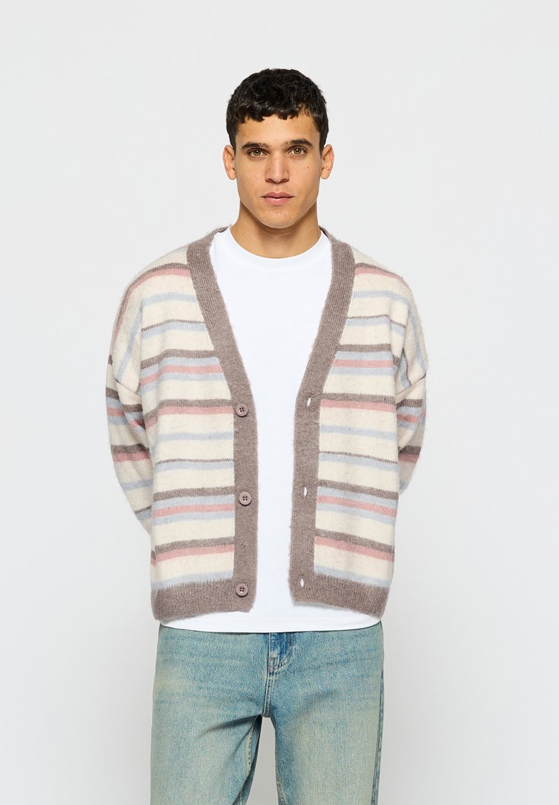 Črtast kardigan iz mehke tkanine, ki ima vodoravne črte v bež, svetlo modri in roza barvi, s svetlo rjavim gumbom spredaj in sproščenim krojem.