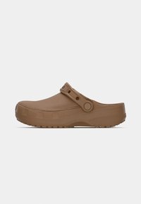 Sabot marron à enfiler avec semelle texturée et bride ajustable positionnée au-dessus du talon sur un fond clair uni.