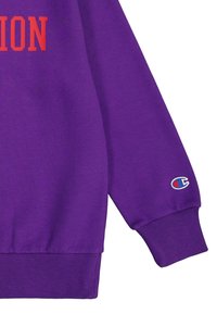 Felpa viola con testo rosso, polsini e orlo a costine. Toppa con logo sulla manica. Tessuto morbido, design rilassato.