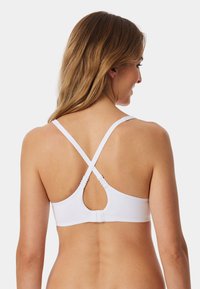 Soutien-gorge de sport blanc avec un design dos nageur, des bretelles croisées et une ouverture en forme de clé à l'arrière. Texture lisse et quincaillerie minimale.