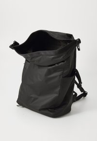 Sort rygsæk lavet af glat, holdbart materiale; har justerbare stropper, en topåbning og sidelommer til ekstra opbevaring.