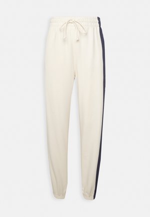 Jogginghosen in Creme mit Kordelzugbund, ausgestattet mit marineblauen Seitenstreifen. Hergestellt aus weichem Stoff, schmal geschnitten mit elastischen Bündchen.
