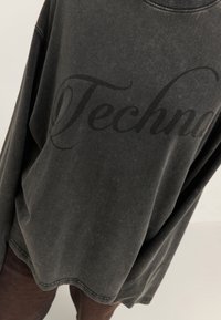 Ylihsize-musta collegepaita pehmeästä kankaasta, jossa on selvästi näkyvä tumma harmaa "Techna"-logo edessä ja ribbetty kaulusyksityiskohta.