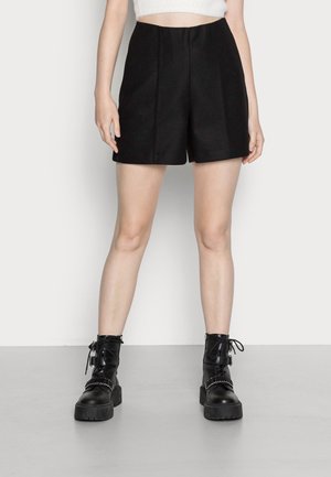 Shorts noirs cintrés avec une taille flatteuse, sans poches, et une texture douce. Associés à des bottines à lacets noires épaisses avec des accents en métal.