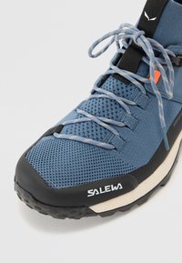 Baskets de sport bleues avec un upper en mesh respirant, accents en caoutchouc noir, semelle intermédiaire beige et lacets contrastants. Présente le logo "SALEWA".