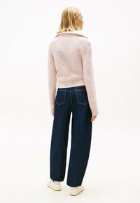 Pull en tricot rose clair avec une texture côtelée et un large col, associé à un jeans large bleu foncé. Le modèle porte des baskets blanches.