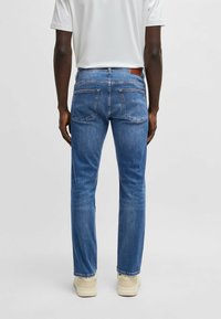 Jeans de denim azul de corte slim, con una textura suave, diseño de cinco bolsillos y un parche de cuero marrón en la cinturilla trasera.