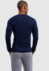 Granatowy sweter z dzianiny z teksturowanym wzorem w warkocze, z długimi rękawami i okrągłym dekoltem, zestawiony z jasnoszarymi dresami.