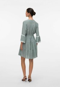 Vestido verde con estampado, mangas de tres cuartos en forma de campana, cintura ajustada y falda acampanada, que presenta una mezcla de diseños geométricos.