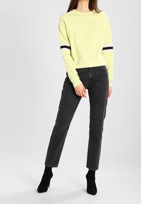 Yellow sweatshirt with black and white stripe accents on sleeves, paired with black tapered jeans and black heeled boots.