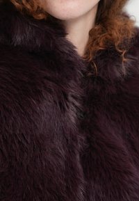 Βαθύ μοβ συνθετική γούνα με απαλή, αφράτη υφή. Ο σχεδιασμός του γιακά δημιουργεί μια ζεστή, αγκαλιαστική εμφάνιση, με παραλλαγές στην απόχρωση.