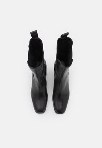 Bottes courtes en cuir noir avec bout carré, doublure textile et languettes pour faciliter l'enfilage ; texture lisse et design minimaliste.