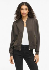 Brun bomberjakke med glidelås foran, ribbestrikkede mansjetter og to glidelåslommer på sidene. Laget av glatt stoff, med gulldetaljer som accent.