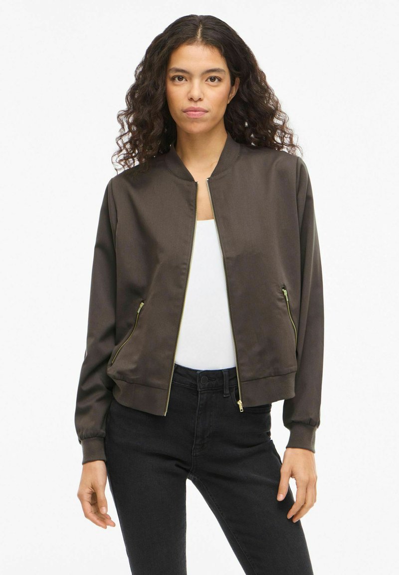 Brun bomberjakke med glidelås foran, ribbestrikkede mansjetter og to glidelåslommer på sidene. Laget av glatt stoff, med gulldetaljer som accent.