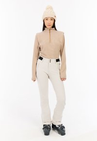 Beige gestreepte lange mouwen top met hoge kraag en halvering rits, gecombineerd met crèmekleurige broeken met zwarte accenten en zakken, sneeuwlaarzen.