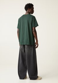 Green cotton t-shirt with short sleeves, relaxed fit. Paired with loose, dark gray denim pants. Minimalist design, no visible patterns or logos.