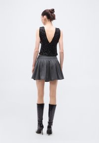 Μαύρο τοπ με παγιέτες και βαθιά V πλάτη, συνδυασμένο με γκρι μίνι πλισέ φούστα με λεπτές κάθετες ρίγες και μαύρες μπότες μέχρι το γόνατο.