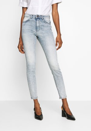 Kvinde iført lyseblå skinny jeans med højtaljede, med falmede detaljer og sorte spidse hæle med slingback.