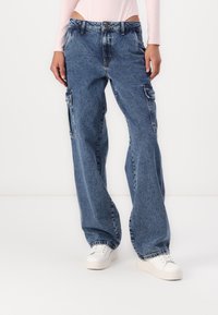 Modre denim cargo hlače z ohlapnim krojem, ki imajo stranske žepe in ravne noge. Obute z belimi športnimi copati.