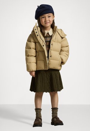 Beige puffer jacket with a high collar and snap buttons, paired with an olive green knitted skirt, brown footwear, and a navy beret.