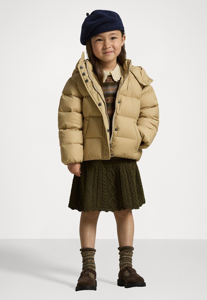 Beige dunjakke med høy krage og trykknapper, kombinert med et olivengrønt strikket skjørt, brune fottøy og en marineblå beret.