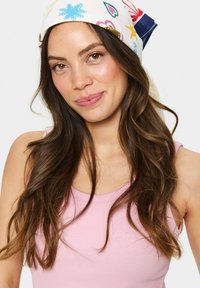 Multicolored scarf with floral and heart patterns, made of lightweight fabric. Soft texture, tied at the back. Model wears a pink tank top.