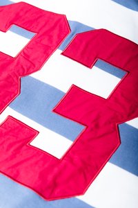 Ένα υφασμάτινο ριγέ σχέδιο με μπλε και λευκές γραμμές, με έναν μεγάλο κεντημένο κόκκινο αριθμό «33» περιγραμματισμένο με κόκκινη ραφή.