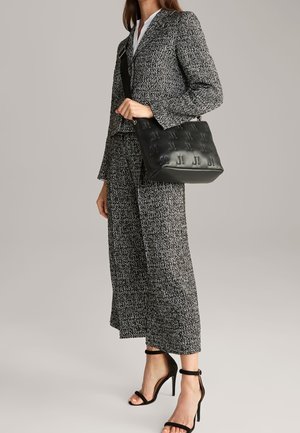 Borsa a spalla in pelle nera con motivo in rilievo, abbinata a un completo in tweed grigio composto da giacca e pantaloni a gamba larga.