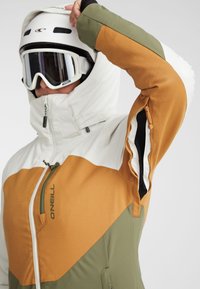 Ski jacket featuring a color-block design in white, brown, and green. Made from textured fabric with zippers and ventilation openings.