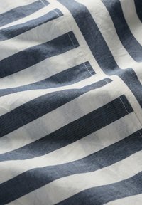 Bawełniana tkanina w naprzemienne pasiaki w granatowym i białym kolorze. Tekstura wydaje się miękka i lekko pomarszczona, z widocznymi detalami szycia.