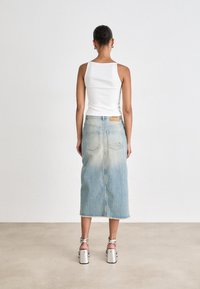 Fustă midi din denim albastru deschis, cu margini desfăcute și buzunare la spate, asortată cu un top alb ajustat și sandale cu toc argintii.