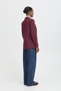 Bordeauxfärgad kavaj med slag, sidofickor och rak skärning, kombinerad med vida blå denimbyxor och bruna skor.