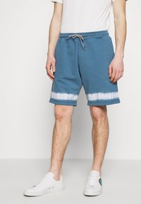 Modré bavlněné kraťasy s bílým tie-dye vzorem na lemu. Elastický pas se šňůrkou, boční kapsy a uvolněný střih.