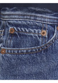 Tejido de mezclilla azul con un bolsillo prominente, remaches de cobre y costuras doradas a lo largo de las juntas, mostrando un tejido texturizado.