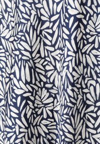 Tissu en coton présentant un motif de feuilles blanches abstrait sur un fond bleu marine, mettant en avant une texture lisse et un contraste de couleurs vives.